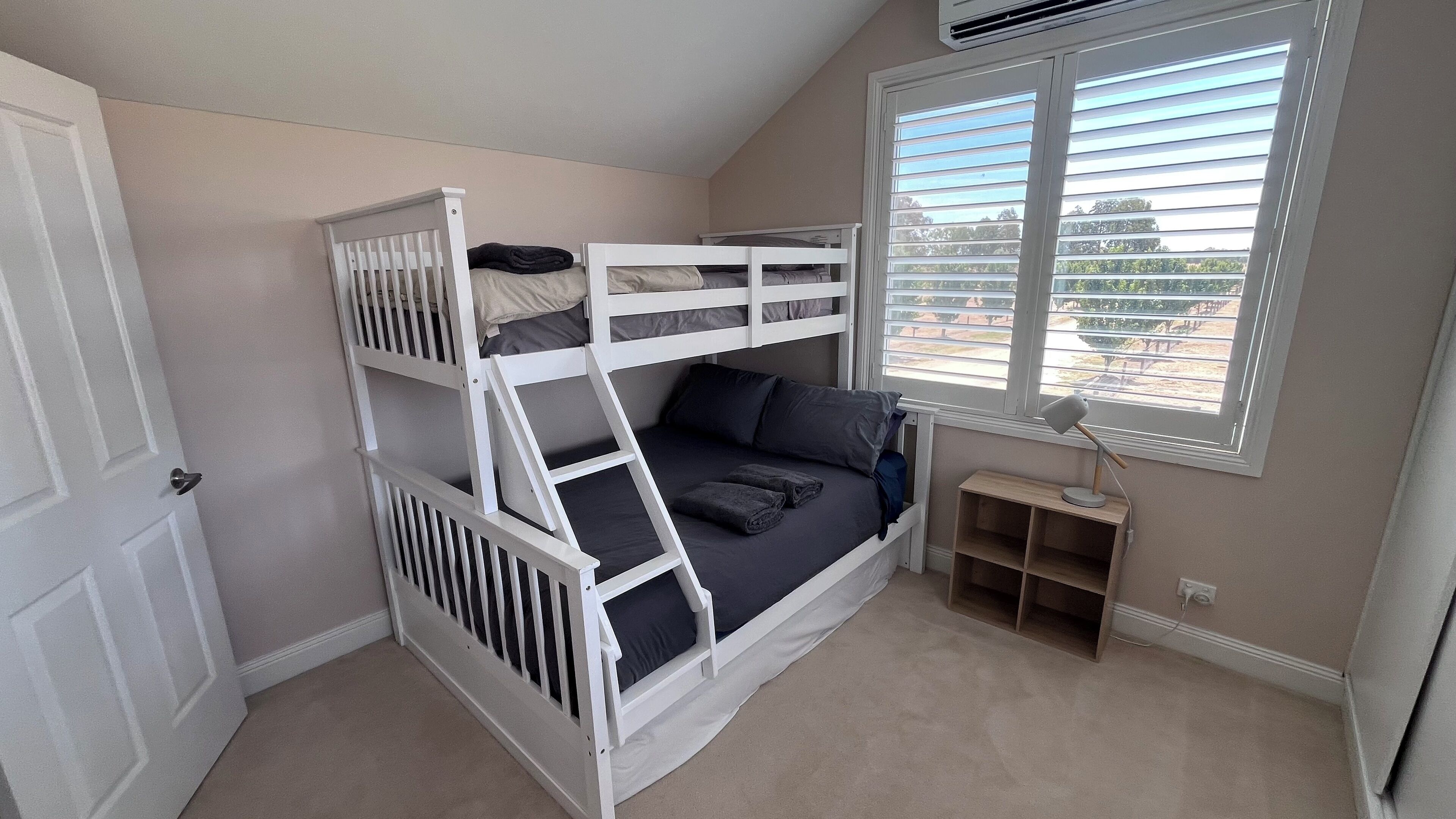 A bunk bed room with a window, a door, and a small shelf.
