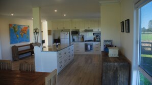 A spacious kitchen with white cabinets, a central island, and a dining area with a wooden table and chairs. - Jackaleah Farm  Stay Oxley (Oxley)