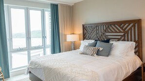 A hotel room with a large bed, a ceiling fan, a window with curtains, and a view of the outdoors. - Tiger's Eye - 2-Bed Luxury Suite with Dramatic Ocean Views (Saint George)
