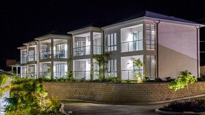 A multi-story building with balconies and large windows, surrounded by a landscaped garden. - Tiger's Eye - 2-Bed Luxury Suite with Dramatic Ocean Views (Saint George)