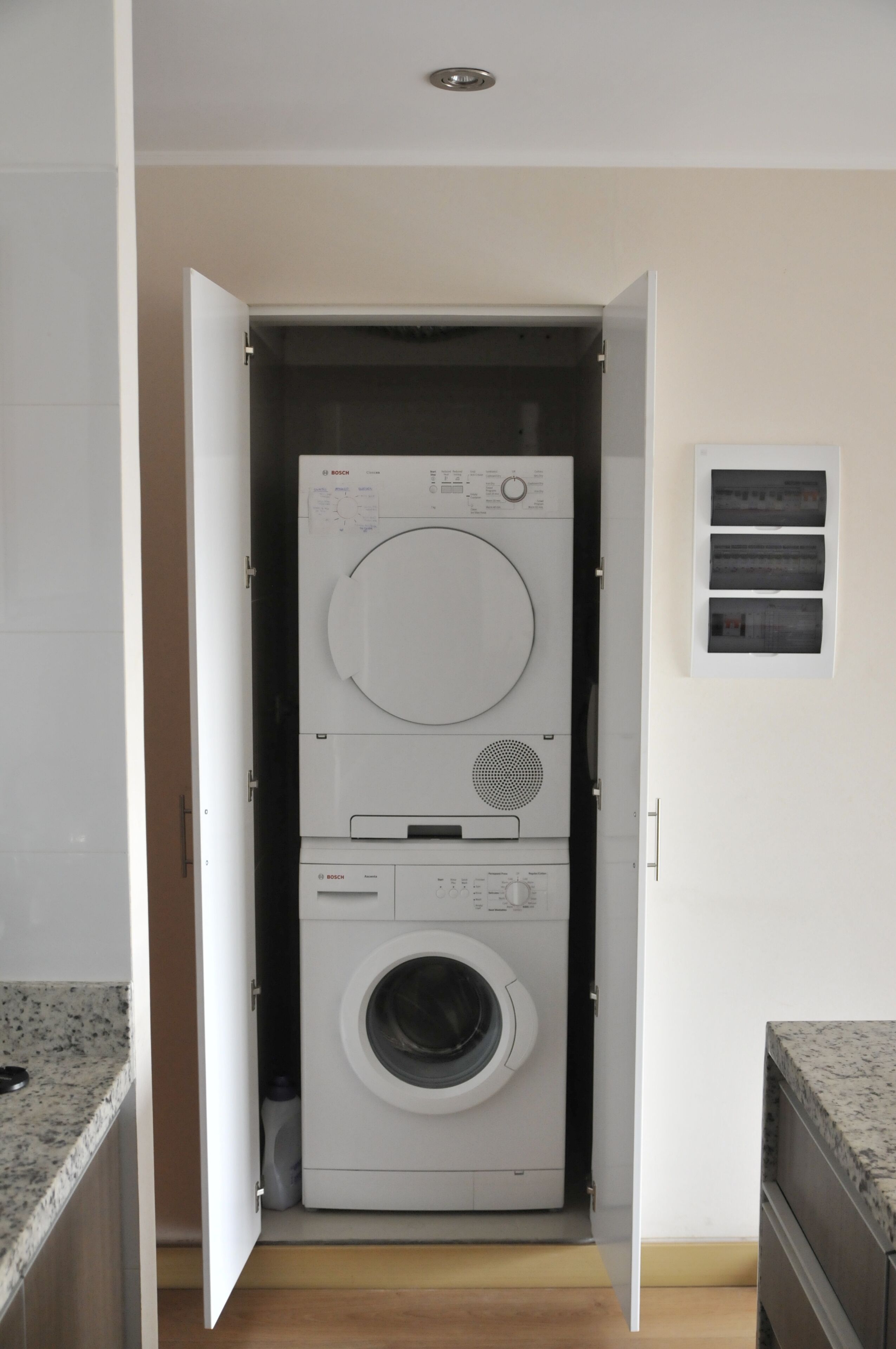 A compact laundry room with a Bosch washing machine and dryer, a small window with a view, and a countertop.