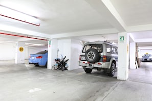 Garagem de estacionamento em vários níveis, com pisos de concreto, paredes brancas e canos vermelhos.