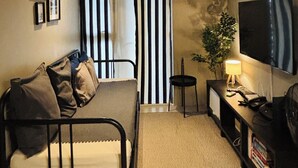 Une chambre à coucher de taille modeste, comprenant un lit, un bureau avec une lampe, un téléviseur et un ventilateur de plafond.