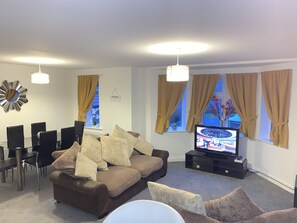 A living room with a brown sofa, a TV, and a dining area with chairs and a table.