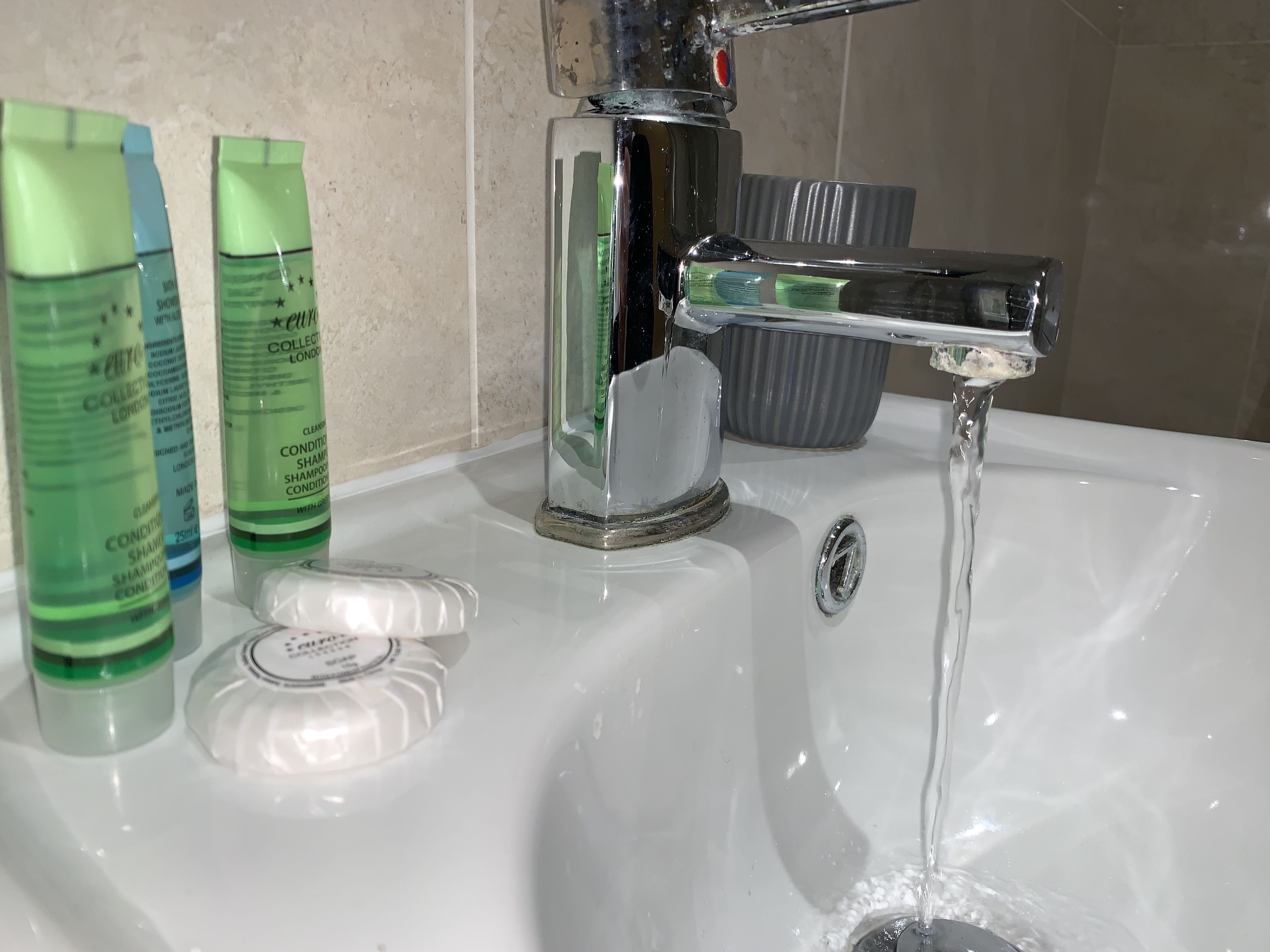 A bathroom sink with running water, a soap dish, and two green bottles of shampoo.