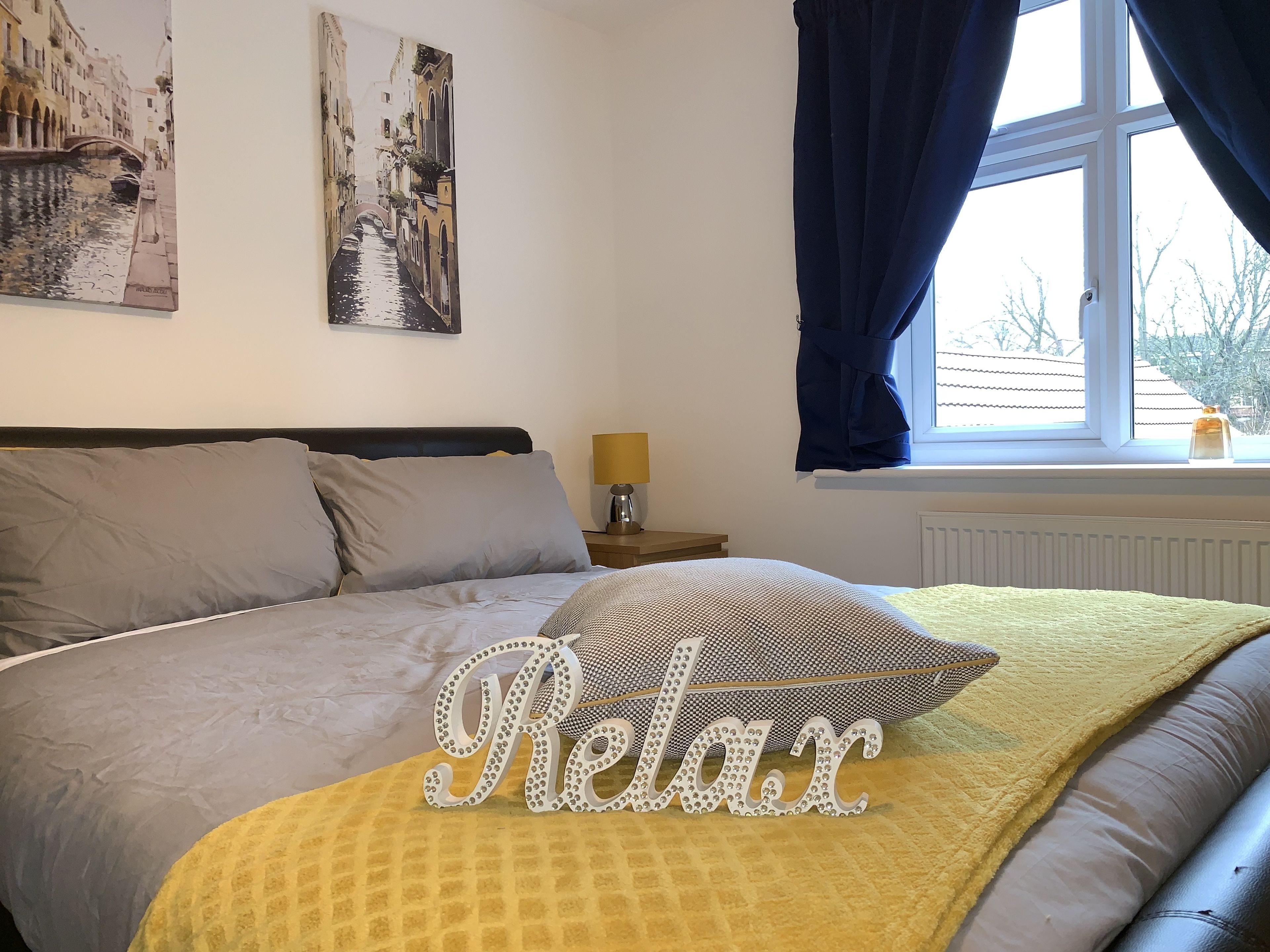 A bedroom with a bed, pillows, a nightstand, a lamp, and a window with curtains.