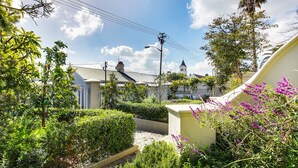 Zona residencial com caminho pavimentado, vegetação exuberante e um edifício com uma torre sineira.