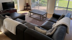A modern living room with a sofa, coffee table, and TV. There is a balcony with a view of greenery. - Relax at "Kangaroo Pause" @ Clayton Bay (Clayton Bay)