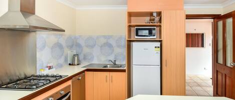 A compact kitchen with a gas stove, oven, stainless steel range hood, a microwave, and a refrigerator.