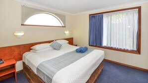 Hotellihuone, jossa on suuri sänky, yöpöytä, työpöytä ja ikkuna, jossa on verhot.