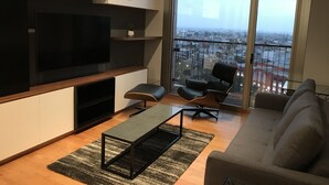 Een moderne woonkamer met een grote televisie, een bank, een fauteuil en een balkon met uitzicht over de stad.