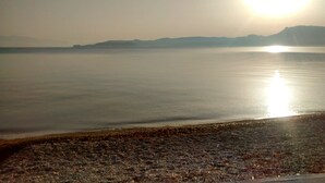 A calm body of water with a rocky shoreline and distant mountains under a clear sky. - Holiday home next to orange tree orchard, 185 sq.m with pool (ΒΟΧΑΣ - ΒΡΑΧΑΤΙΟΥ)