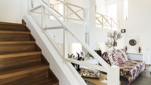 A staircase with wooden steps and white railings leading to a room with a patterned sofa and a small table with decorative items. - Holiday home next to orange tree orchard, 185 sq.m with pool (ΒΟΧΑΣ - ΒΡΑΧΑΤΙΟΥ)