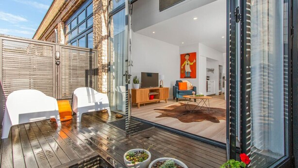 A modern living room with a glass door leading to a kitchen and dining area. - City Fringe Converted Industrial Townhouse (Auckland)