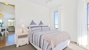 A bedroom with a bed, bedside tables, a ceiling fan, and a window with curtains. - Sunset at Snapper Point ~ Aldinga Beach - Modern Coastal Beauty with Large Balcony and Sea Views (Aldinga Beach)