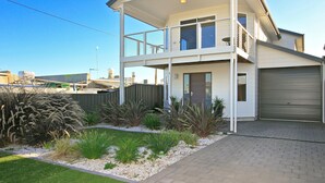 A two-story house with a covered balcony, a garage, and a landscaped garden. - Sunset at Snapper Point ~ Aldinga Beach - Modern Coastal Beauty with Large Balcony and Sea Views (Aldinga Beach)