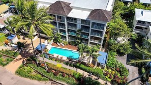 Hotel de vários andares com piscina, rodeado por palmeiras e jardins bem cuidados.