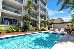 Um edifício moderno com piscina, espreguiçadeiras e plantas tropicais.