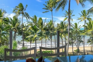 Vista sulla spiaggia con palme, una recinzione di legno e un tavolo con sedie.