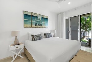 Quarto com cama grande, mesa de cabeceira, uma obra de arte na parede e porta de vidro deslizante para uma varanda.