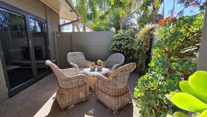 Un patio con mobiliario de mimbre y dos cactus en macetas.
