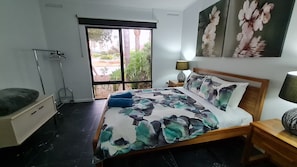 Un dormitorio con cama, mesita de noche, lámpara, ventana y vistas al exterior.