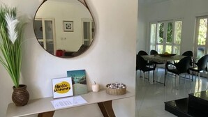 Una sala de estar moderna con un espejo redondo, una mesita baja con adornos, y un comedor con sillas y una mesa.