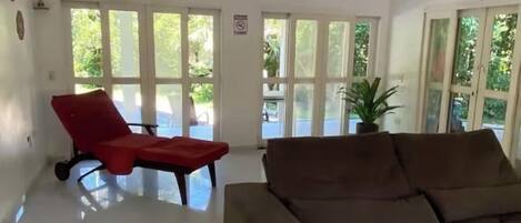 Un amplio salón con un sofá seccional grande, un sillón rojo y un ventilador de techo.