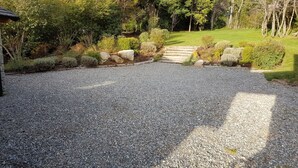 Un camino de grava que conduce a una escalera de madera rodeada de abundante vegetación y árboles.