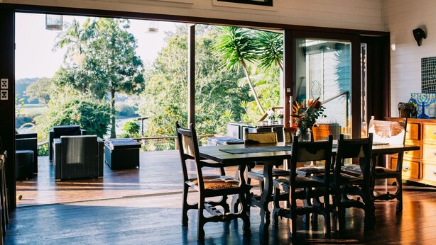 A spacious dining area with a large table and chairs, a view of lush greenery outside, and a wooden deck. - BELLINGEN CONVERTED CHURCH on the river (Fernmount via Bellingen)