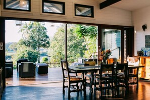 Un comedor amplio con una gran mesa y sillas, vistas a exuberante follaje y una terraza de madera.