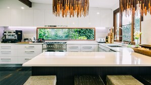 A modern kitchen with white cabinetry, a large island, and a hanging wooden light fixture. - BELLINGEN CONVERTED CHURCH on the river (Fernmount via Bellingen)