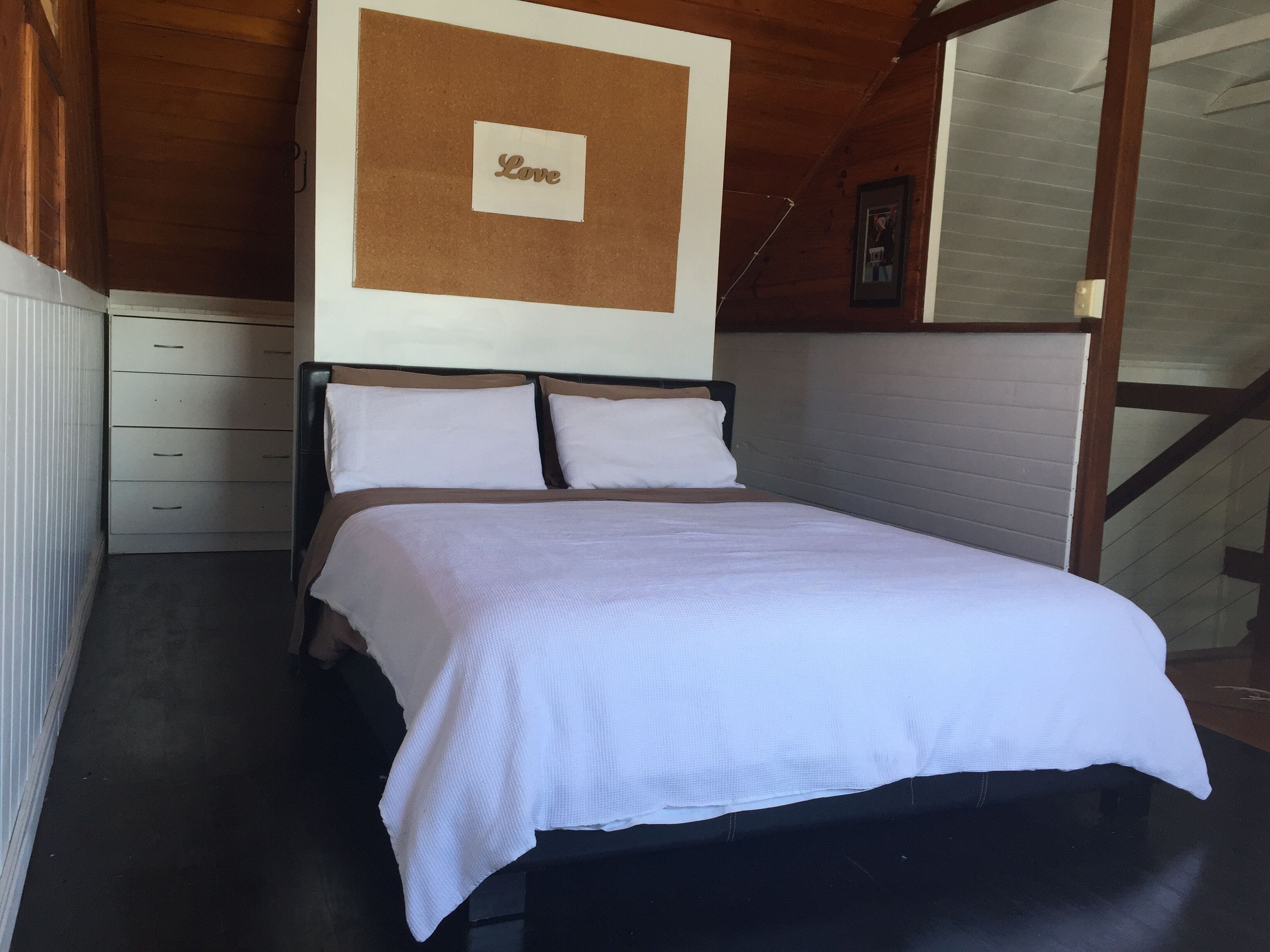 Ein ordentlich bezogenes Bett in einem Zimmer mit Holzboden und einem an der Wand befestigten Schild mit der Aufschrift 'Love'.