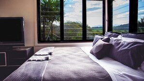 A bedroom with a large window, a bed with pillows, and a TV on a stand. - BELLINGEN CONVERTED CHURCH on the river (Fernmount via Bellingen)