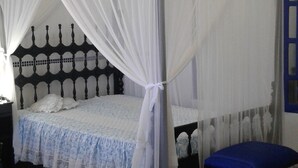 Une chambre avec un lit à baldaquin, un banc bleu et des carreaux de sol à motifs.