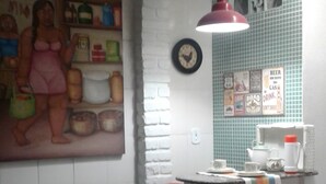 Une cuisine avec un mur en briques blanches, un luminaire suspendu rouge, une horloge et un pare-feu en carreaux orné de divers motifs.