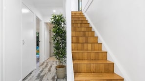 A modern interior with a wooden staircase, a hallway with a patterned floor, and a potted plant. - Graebill - Light & Spacious Duplex (SUNSHINE BEACH)