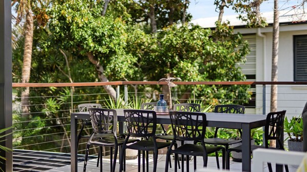 Un área de comedor al aire libre con una mesa y sillas, rodeada de follaje y una barandilla.