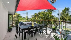Relax on the balcony overlooking a lush tropical garden with a shaded seating area and a metal railing.