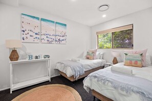 A bedroom with two beds, a nightstand, a desk, and a window with a view of trees. - Peregian Beach Apartment (Peregian Beach)