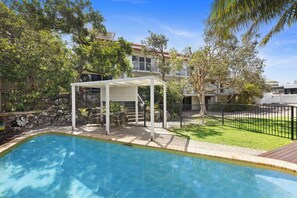 A swimming pool with a covered seating area, surrounded by a fenced yard and trees. - Peregian Beach Apartment (Peregian Beach)
