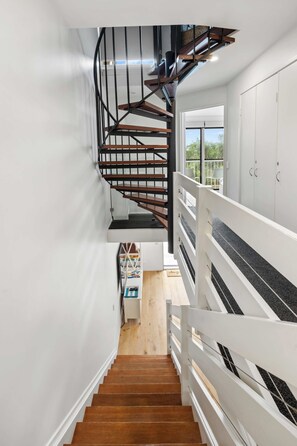 A modern staircase with a wooden finish and metal railings, leading to a room with white walls and a view of the outdoors. - Peregian Beach Apartment (Peregian Beach)