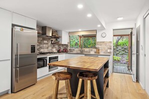 Een moderne keuken met een centraal eiland, roestvrijstalen apparatuur en uitzicht op een tuin.