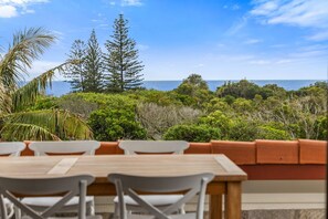 An outdoor dining area with a view of the ocean, surrounded by dense greenery and trees.