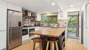 Een moderne keuken met een groot eiland, roestvrijstalen apparatuur en uitzicht op groen.