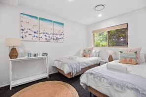 A bedroom with two beds, a bedside table, a lamp, and beach-themed wall art.