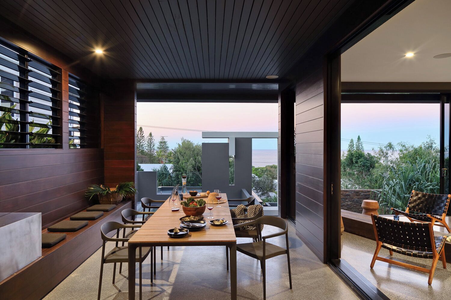 A modern dining area with a long table, chairs, and a view of the outdoors.