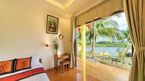 A hotel room with a bed, desk, and a view of a lake and palm trees.