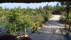A pathway leading to a water body, surrounded by lush greenery and a covered area with chairs.