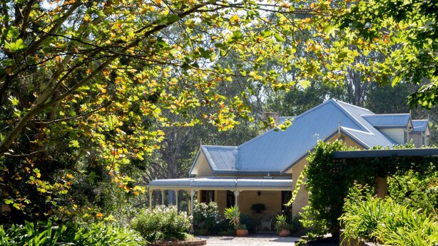 A house with a covered porch, surrounded by lush greenery and trees.